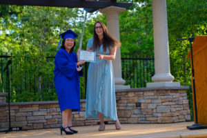 Graduate in cap and gown receiving diploma from teacher
